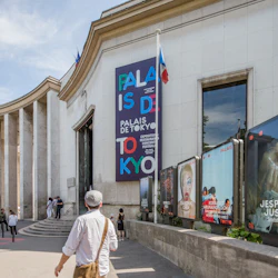 En modern byggnad med skylten "Palais de Tokyo" och annonser utanför, människor som går nära den, under en solig himmel.