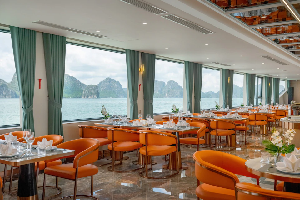 Modern dining area with orange chairs, neatly set tables, large windows offering scenic views of mountains over water.