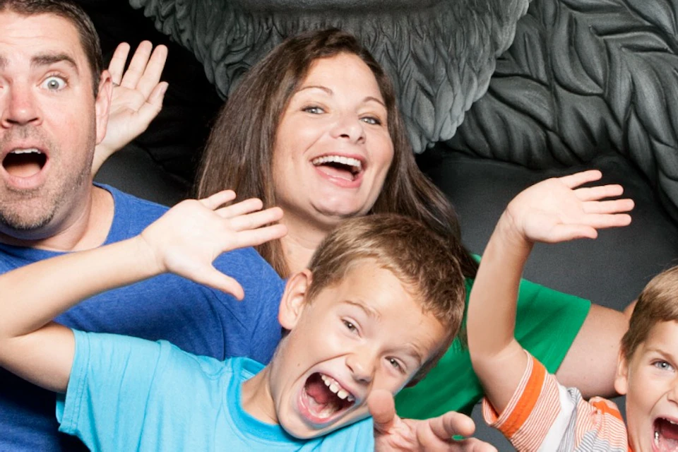 A family posing excitedly inside the arms of a large King Kong sculpture, with the ape's mouth open wide behind them.