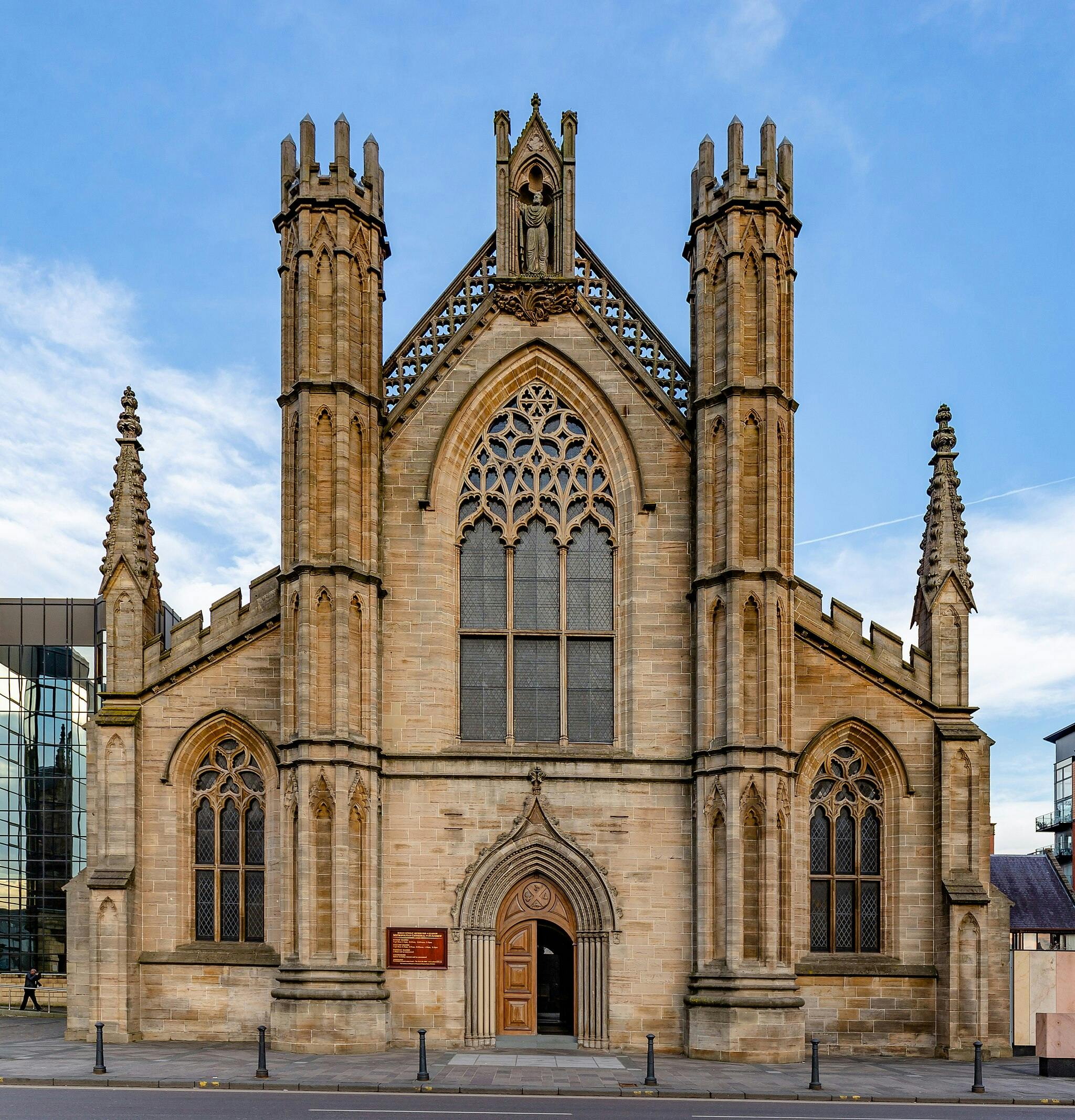 A gothic-style stone building with large arched windows, ornate detailing, and two tall towers, set against a blue sky.