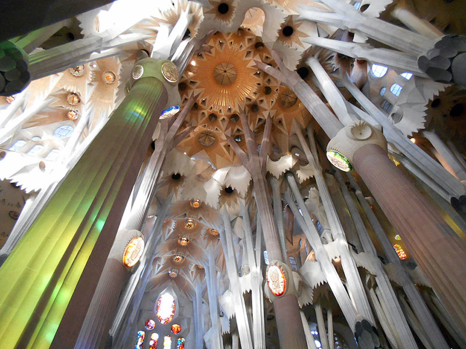Intricate architectural ceiling with vertical columns and colourful stained glass windows in a grand interior space.