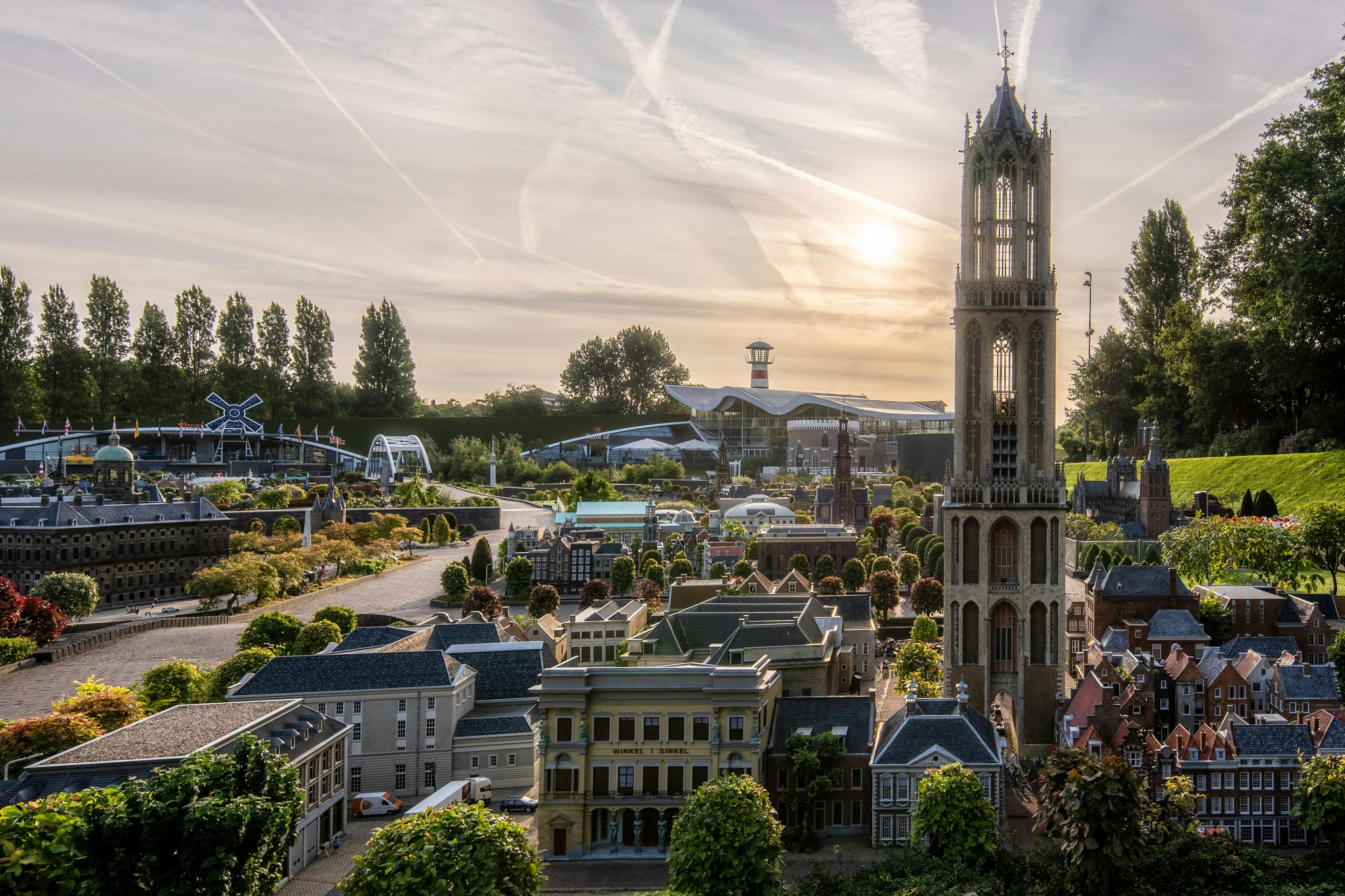 부분적으로 흐린 하늘 아래 디테일한 건물, 높은 타워, 주변 녹지가 있는 미니어처 도시 풍경입니다.