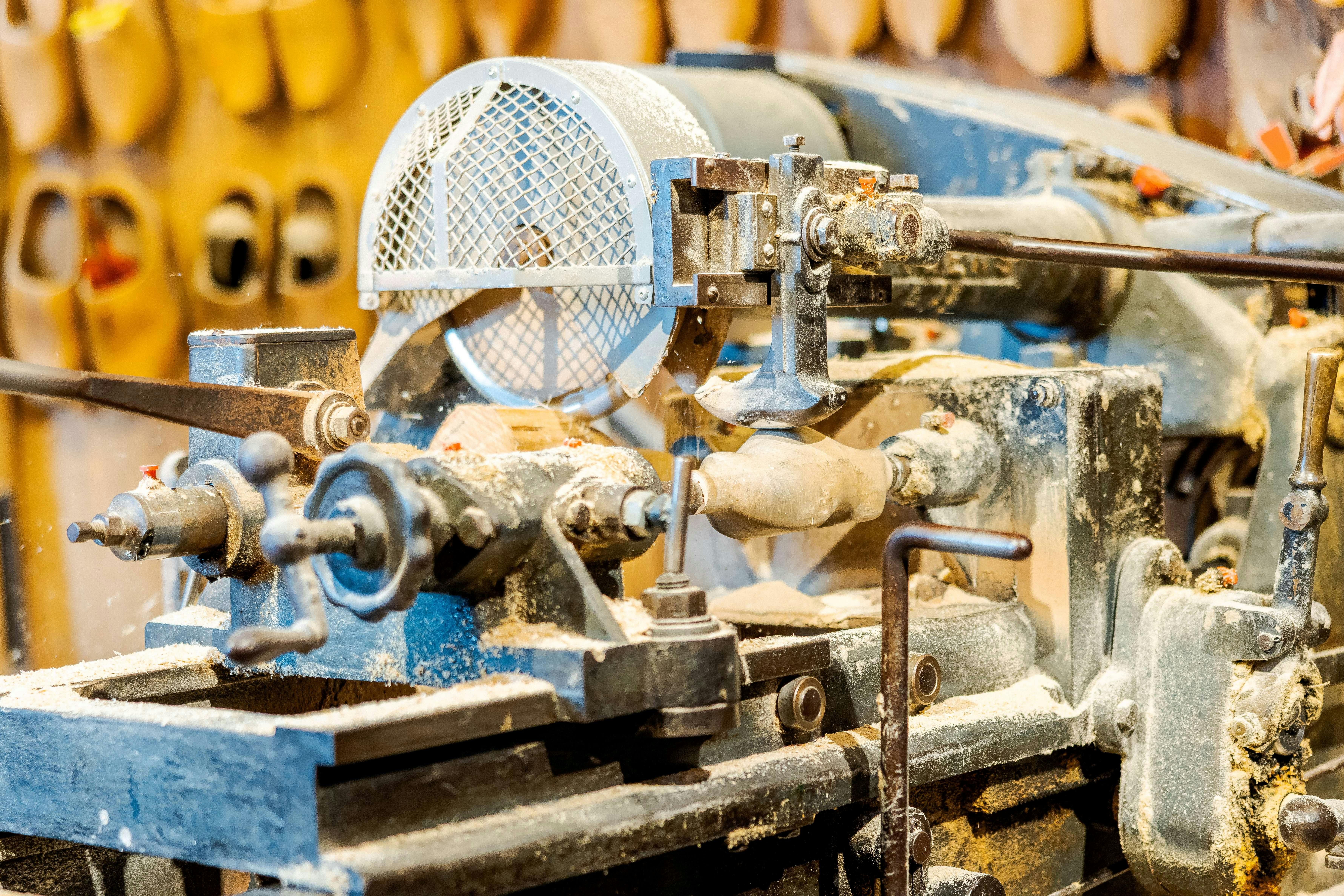 Κοντινό πλάνο μηχανής τόρνου σε χρήση, που διαμορφώνει ένα ξύλινο κομμάτι. Τα ροκανίδια και η σκόνη απλώνονται γύρω από το μηχάνημα.