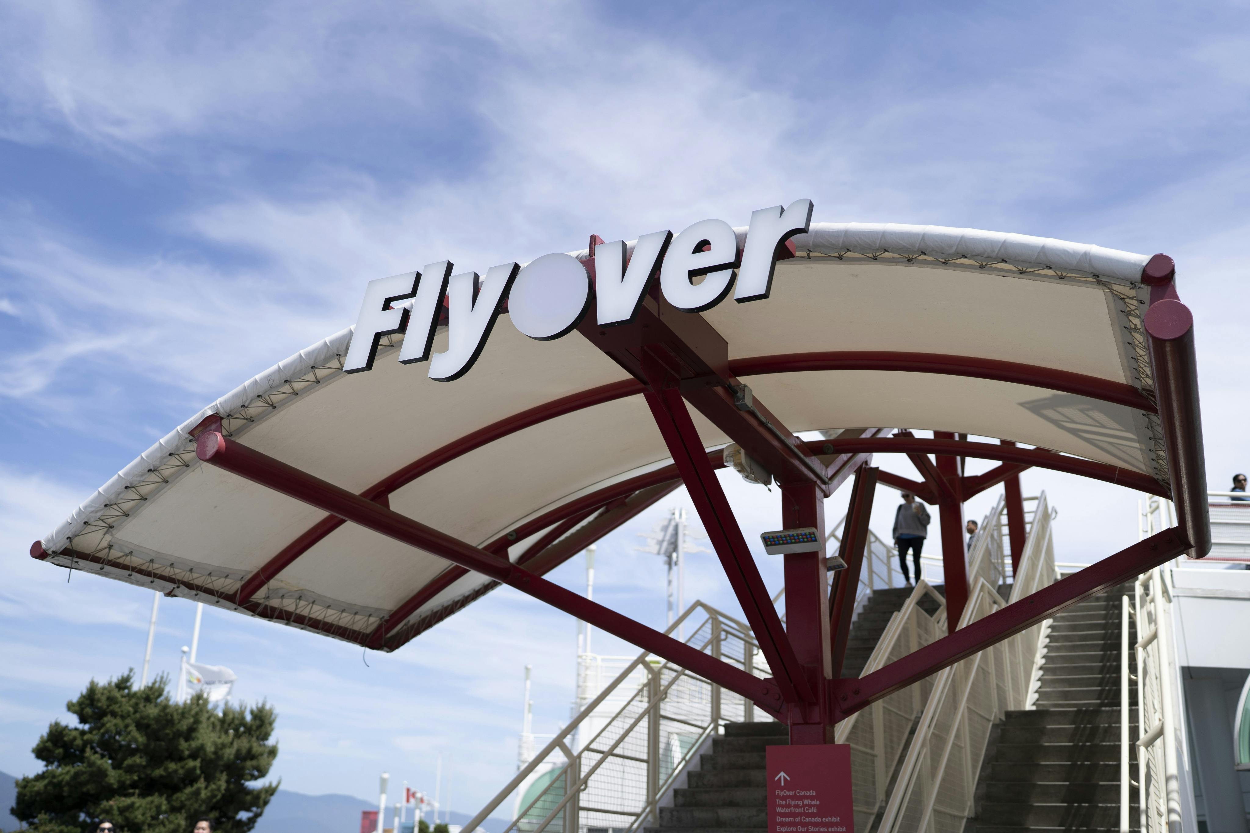 A canopy structure with the word 'Flyover' displayed on top. Stairs and a person ascending are visible in the background.