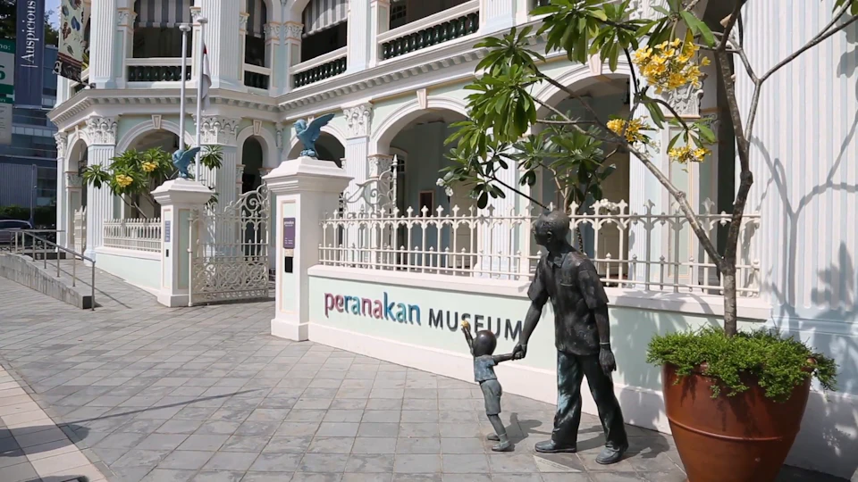 Exterior of the Peranakan Museum with bronze statues of a man and child holding hands near the entrance gate.