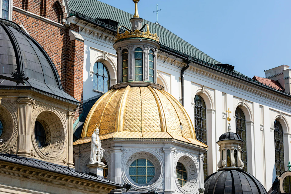 A golden-domed building with intricate architectural details and surrounding structures under a clear blue sky.