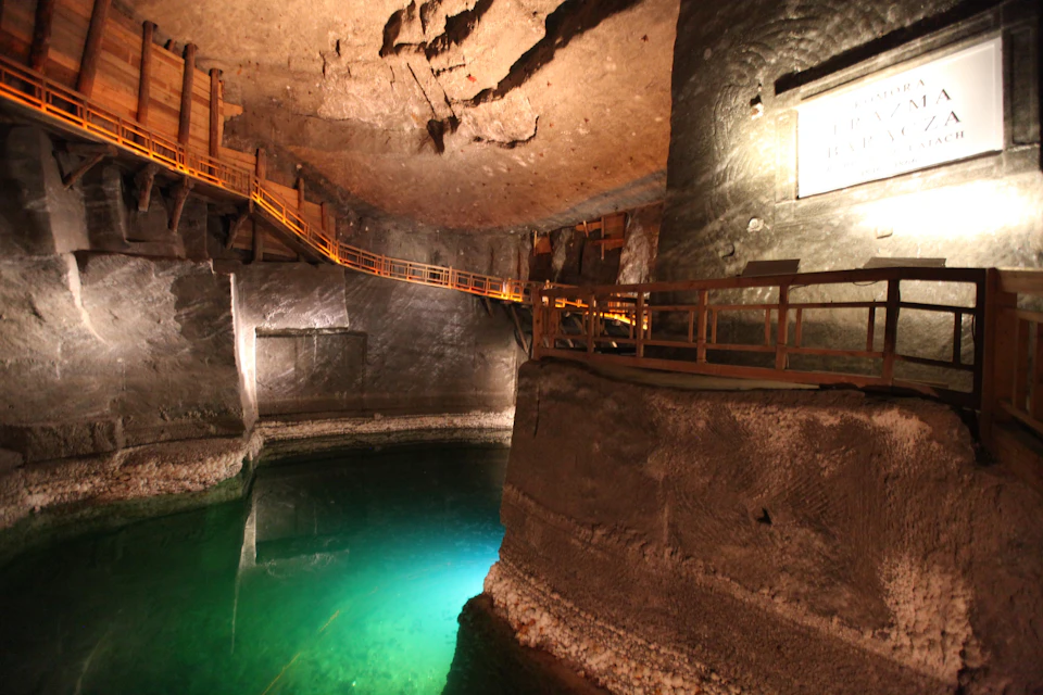 Underground cavern with illuminated green water, surrounded by rock walls and wooden walkways.