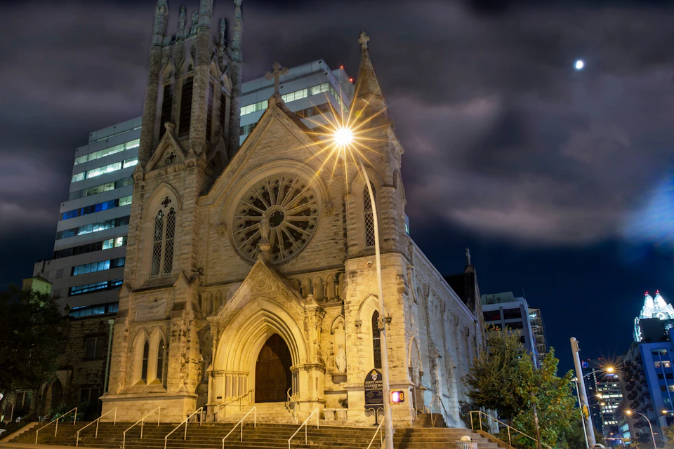 Tall church cathedral at night with a light shining from behind it.