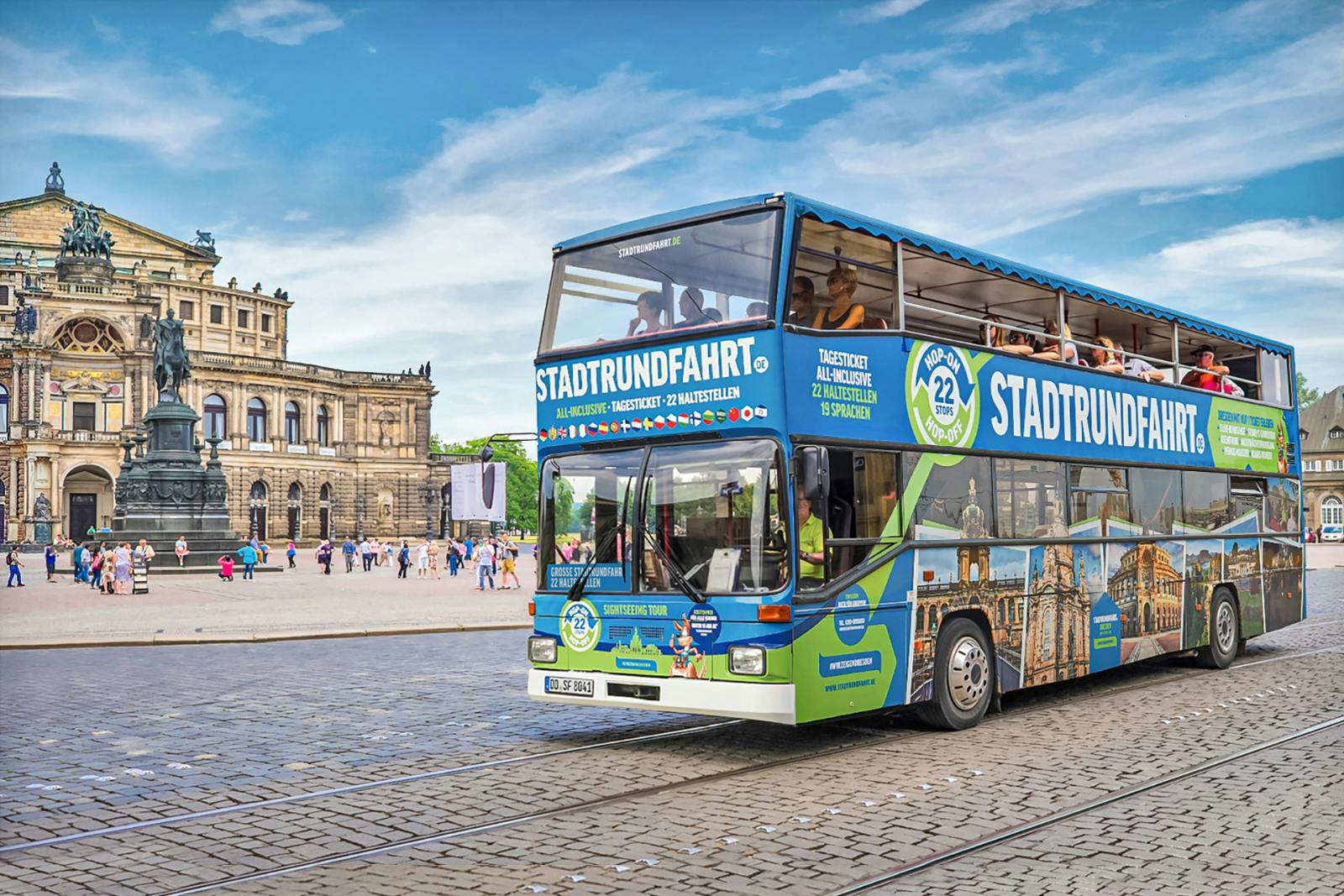 A double-decker tour bus labeled "STADTRUNDFAHRT" drives in front of a historic building in a cobblestone plaza.