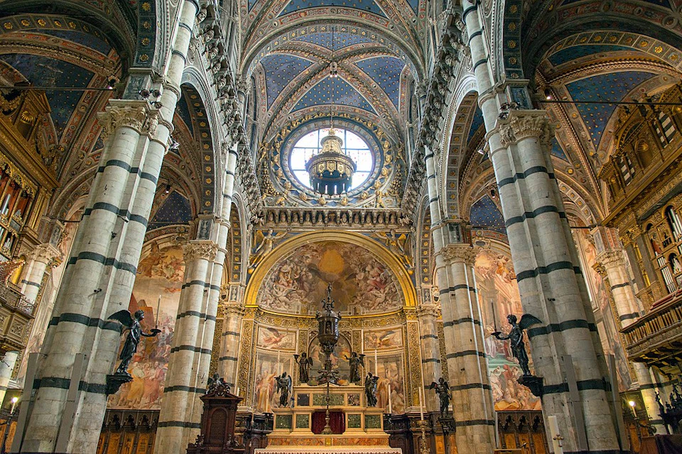 Ornate cathedral interior with tall, striped columns, intricate ceiling arches, and detailed frescoes above an elaborate altar.