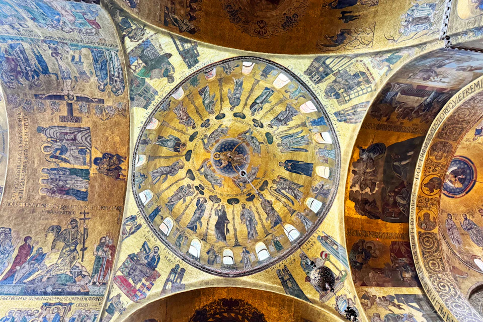 Interior view of a dome with intricate mosaics depicting religious figures and scenes, illuminated by warm light.
