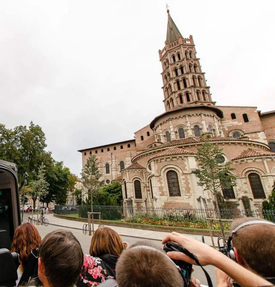 A group of people wearing headphones look at a historic church with a tall, ornate tower set against a cloudy sky.
