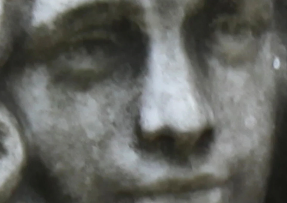 A stone statue of a seated woman, leaning on one hand, surrounded by gravestones and columns in a cemetery.
