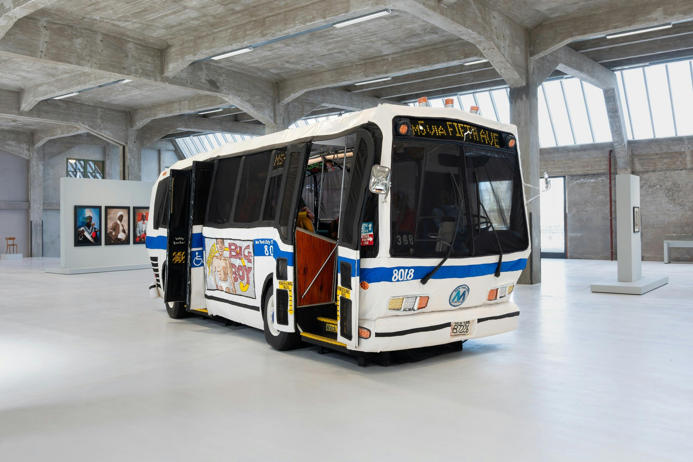 En hvid og blå bus udstillet indendørs, modificeret med en bøjet form, under moderne industriel arkitektur.
