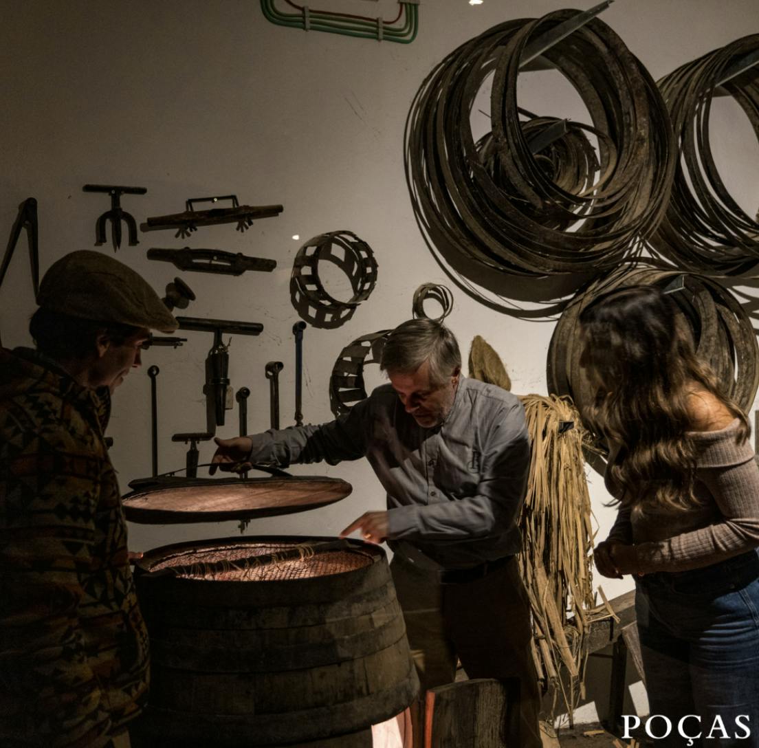 Tres personas examinan un barril en un taller con herramientas y piezas de ruedas colgadas de las paredes.