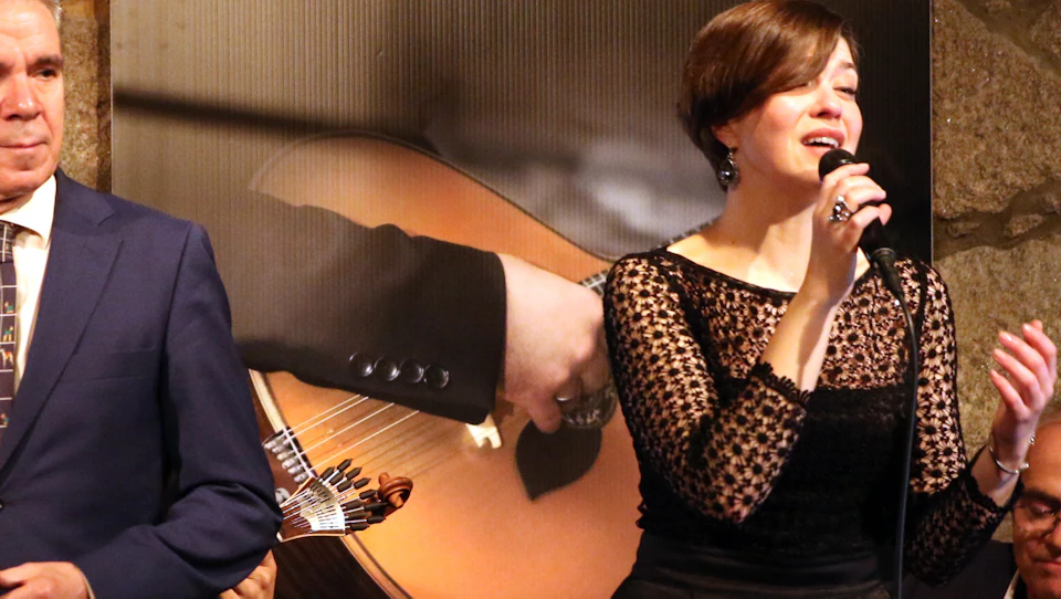 A woman is singing while a man stands beside her, and a poster in the background reads "Fado in Porto" and "Porto Calem."