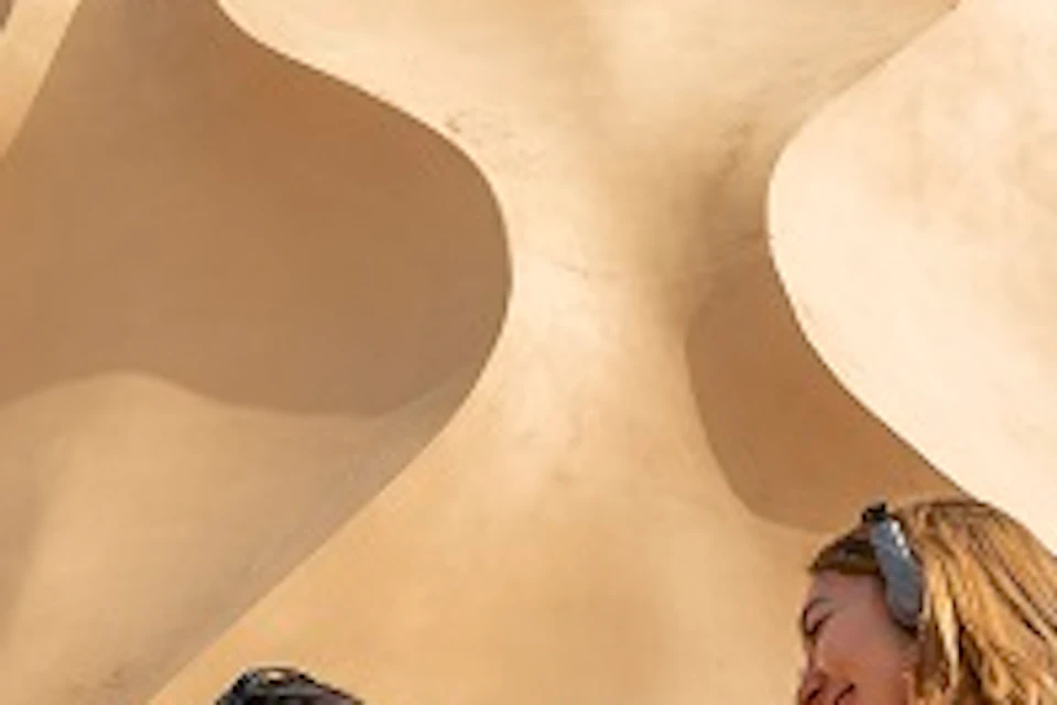 Four people with headphones stand and chat in front of a unique architectural structure with organic shapes, under a clear sky.