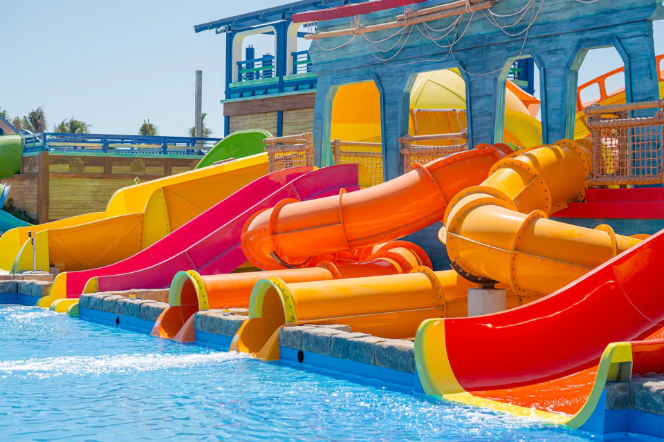 Brightly colored water slides and tubes at a water park, with a pool at the bottom under a clear blue sky.