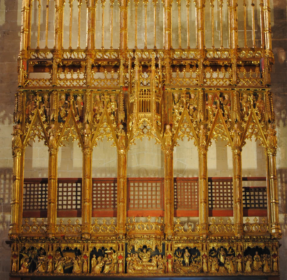 An ornate golden altarpiece with intricate Gothic design, featuring arches, religious figures, and detailed carvings.