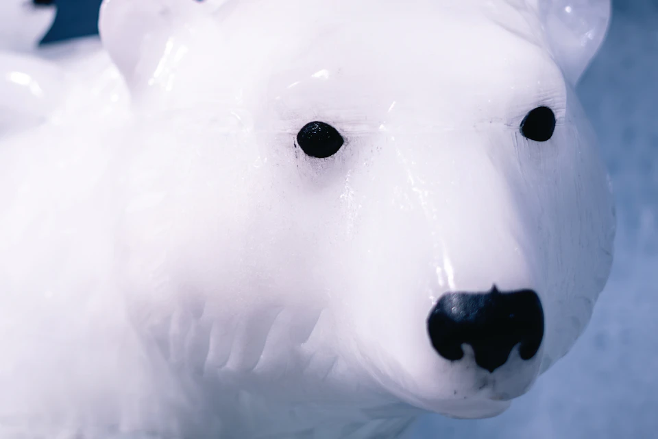Close-up of a polar bear ice sculpture, with another smaller polar bear sculpture in the background, set against an icy backdrop.