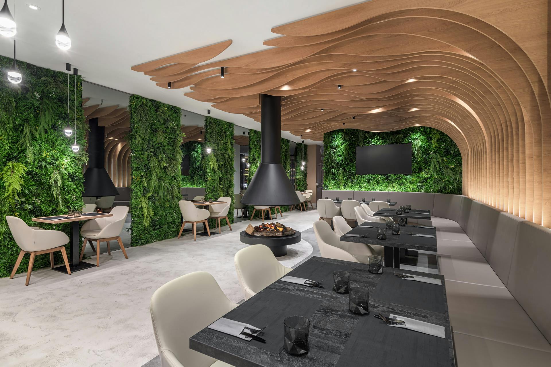 Modern restaurant with green walls, wavy wooden ceiling, table settings, and white chairs. Central fireplaces and plant decor.