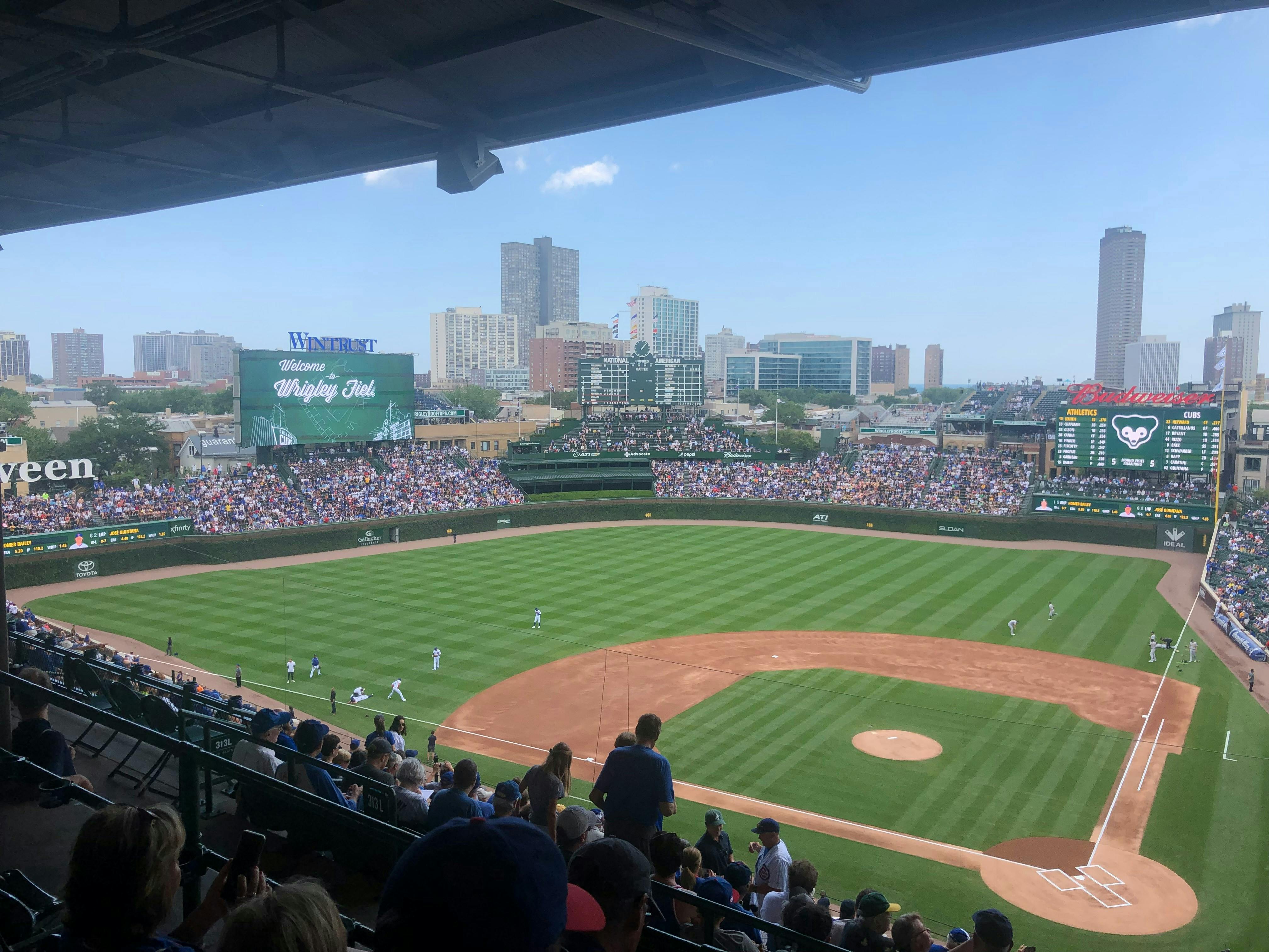 Wrigley Field während eines Baseballspiels, überfüllte Tribünen, Spieler auf dem Spielfeld und die Anzeigetafel mit der Aufschrift "Welcome to Wrigley Field".
