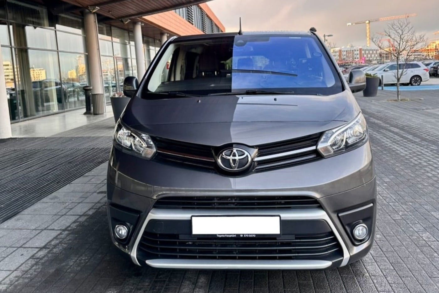 회색 도요타 미니밴은 커다란 창문과 나무 돌출부가 있는 현대적인 건물 외부에 주차되어 있습니다.