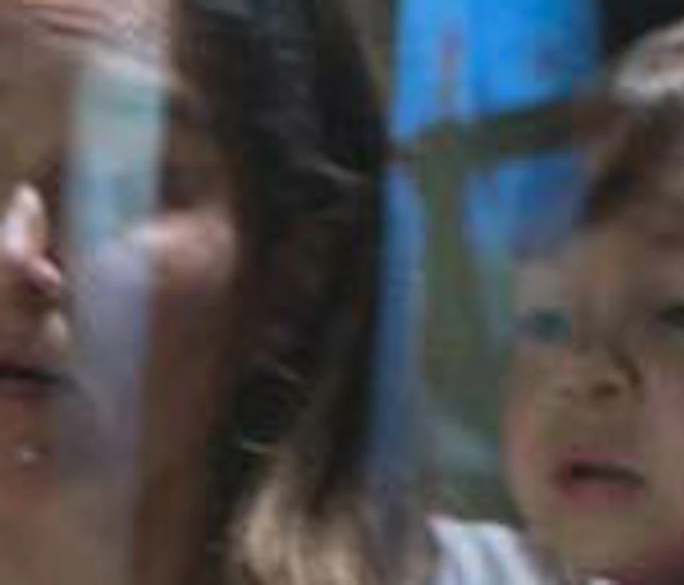 A woman holding a child looks at a detailed miniature model of a medieval castle in a museum setting.
