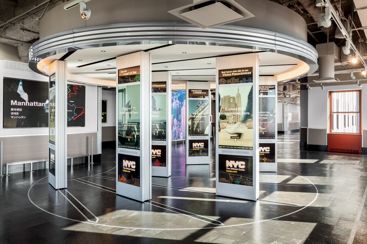 Un moderno spazio interno con pannelli informativi sulle attrazioni di New York e immagini illuminate del paesaggio urbano.