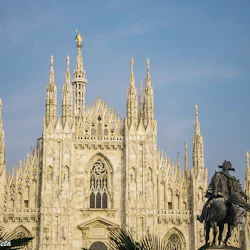 Gotisk katedral med utsmyckade spiror i bakgrunden och en ryttarstaty i förgrunden under en klarblå himmel.