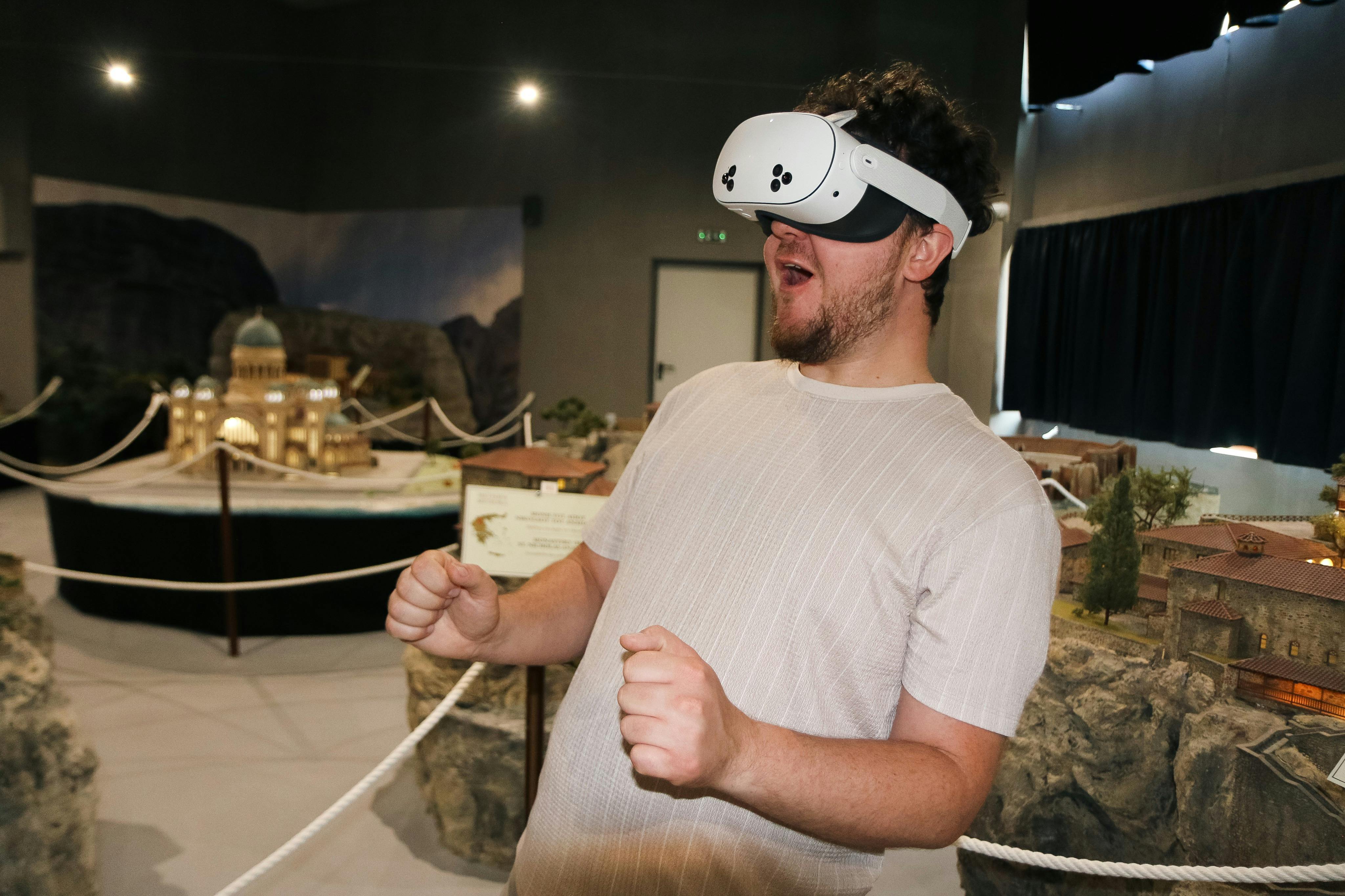 A person wearing a virtual reality headset appears excited, with hands clenched, in a room displaying various models and exhibits.