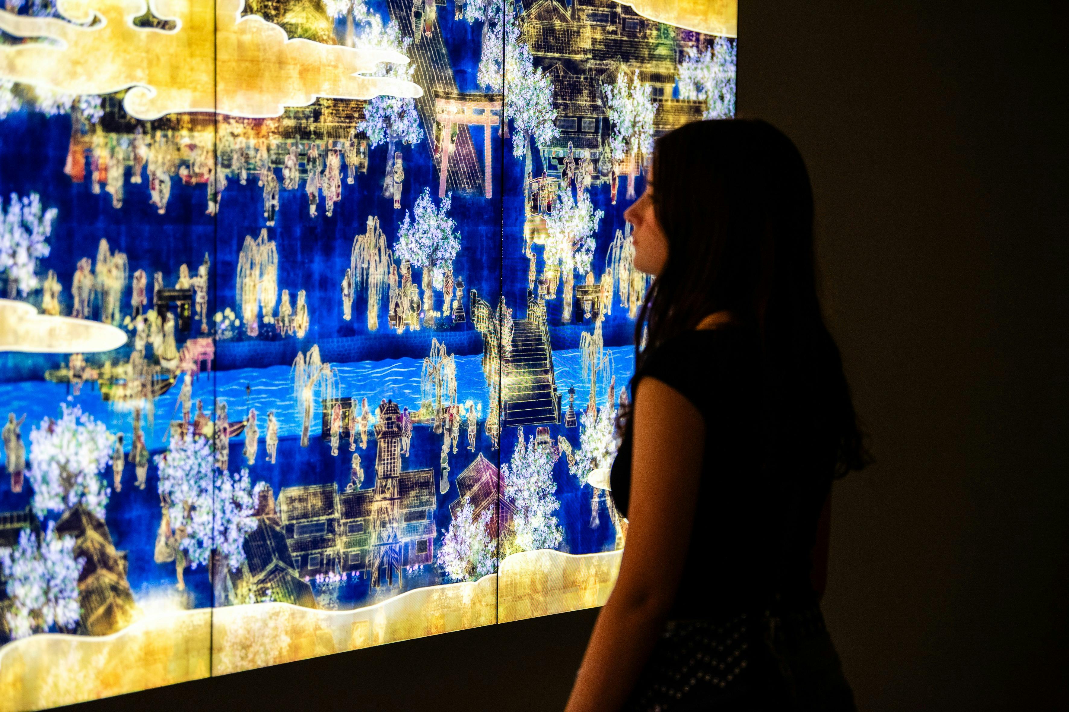 Osoba stoi przed jaskrawo oświetlonym dziełem sztuki z misternymi wzorami i żywymi kolorami.