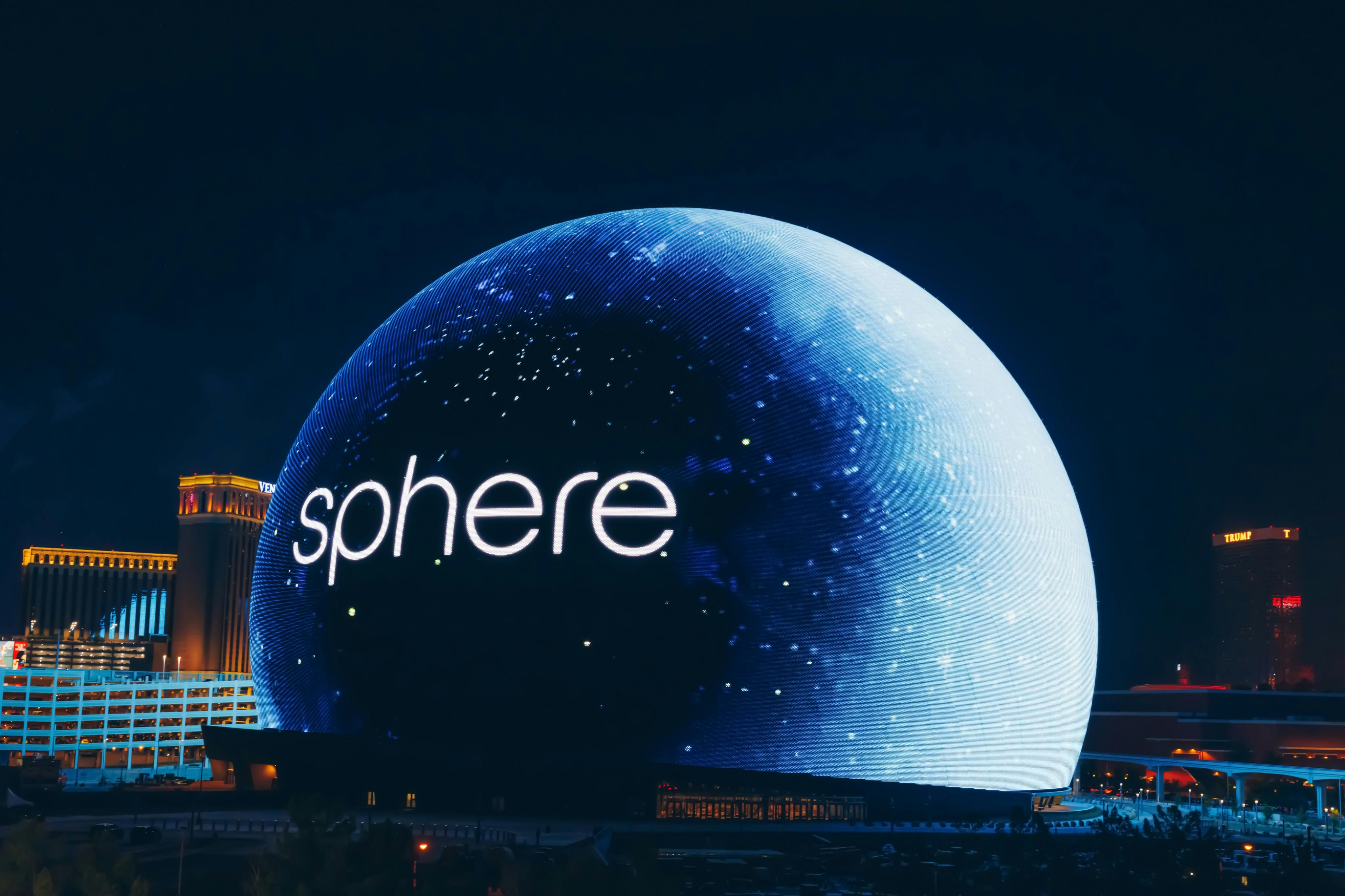 A large spherical building illuminated with the word "sphere" and starry patterns against a dark night sky.
