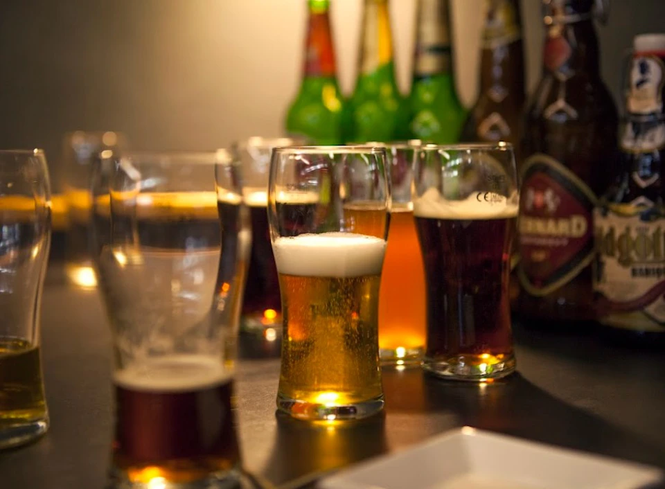 Various glasses of beer and beer bottles on a table, with different types and colors of beer visible.