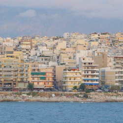Flera mellanhöga flerbostadshus vid vattnet, med berg i bakgrunden och en stenstrand i förgrunden.
