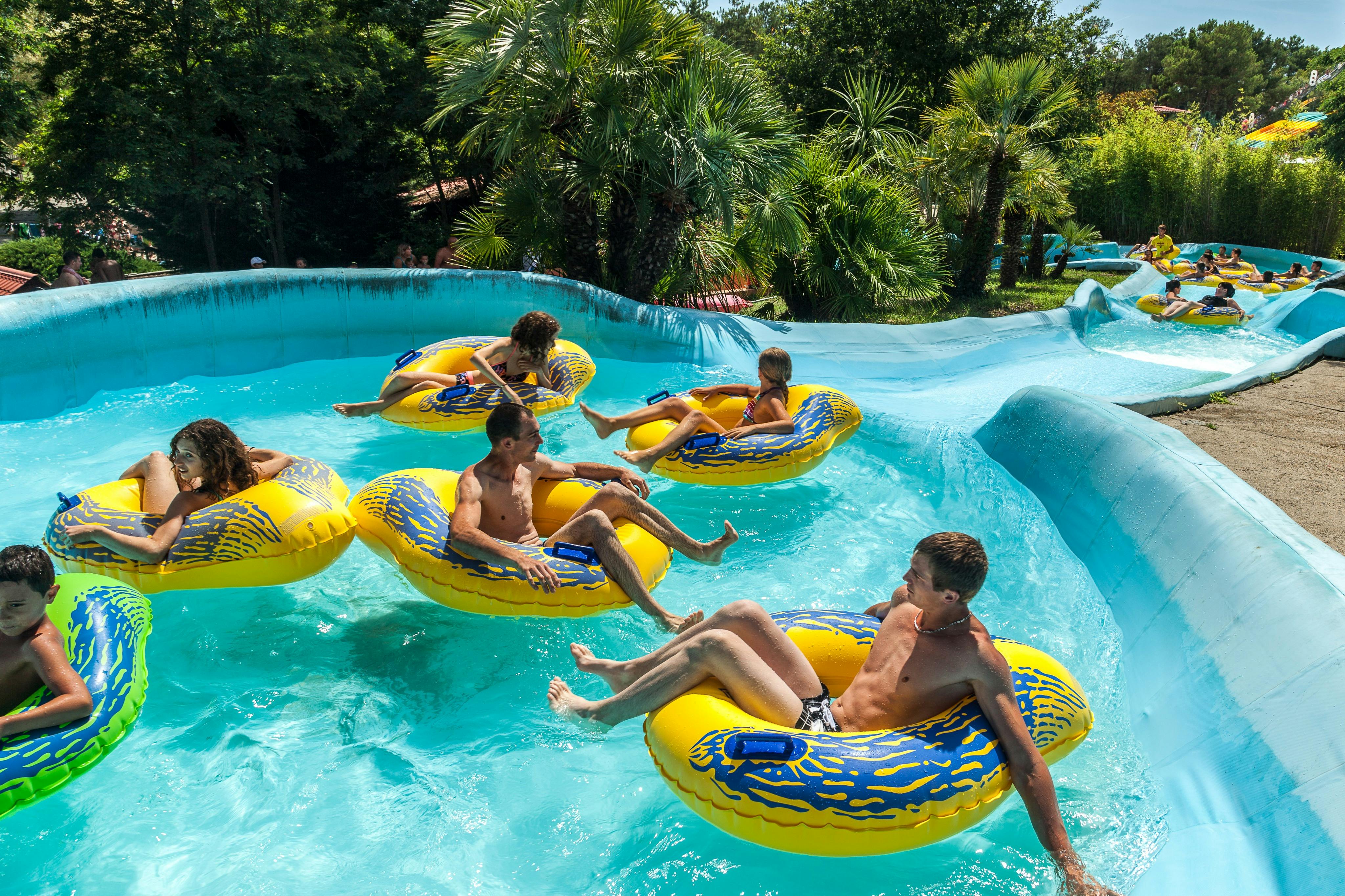 Des personnes s'amusant sur une attraction aquatique à bord de bouées gonflables colorées dans un parc aquatique à thème tropical.
