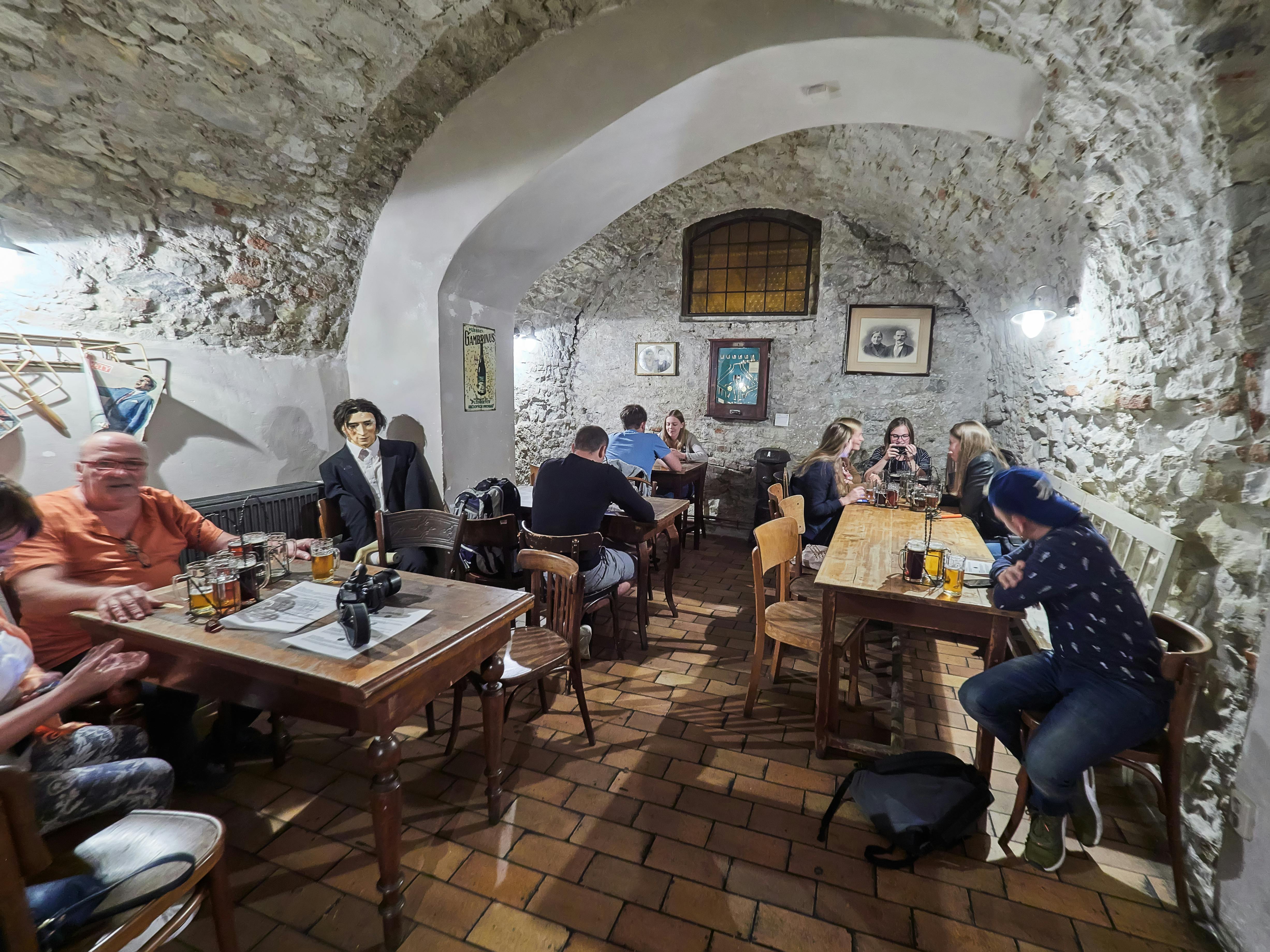 Gezellig restaurant met stenen muren en gewelfd plafond, klanten zitten aan houten tafels, kletsen en genieten van eten en drinken.