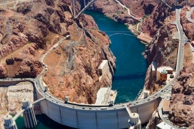 Aerial view of a large dam spanning a river in a canyon, with roads and structures built into the surrounding landscape.