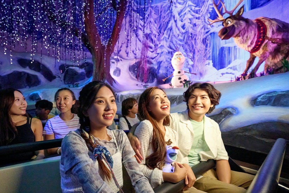 Un grup de persones gaudeix d'un passeig en una atracció amb temàtica d'hivern amb llums parpellejants i un personatge d'un ninot de neu.