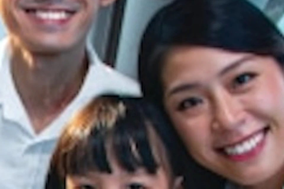 A smiling family of three sits inside a glass cable car with a scenic view of water, boats, and city buildings in the background.