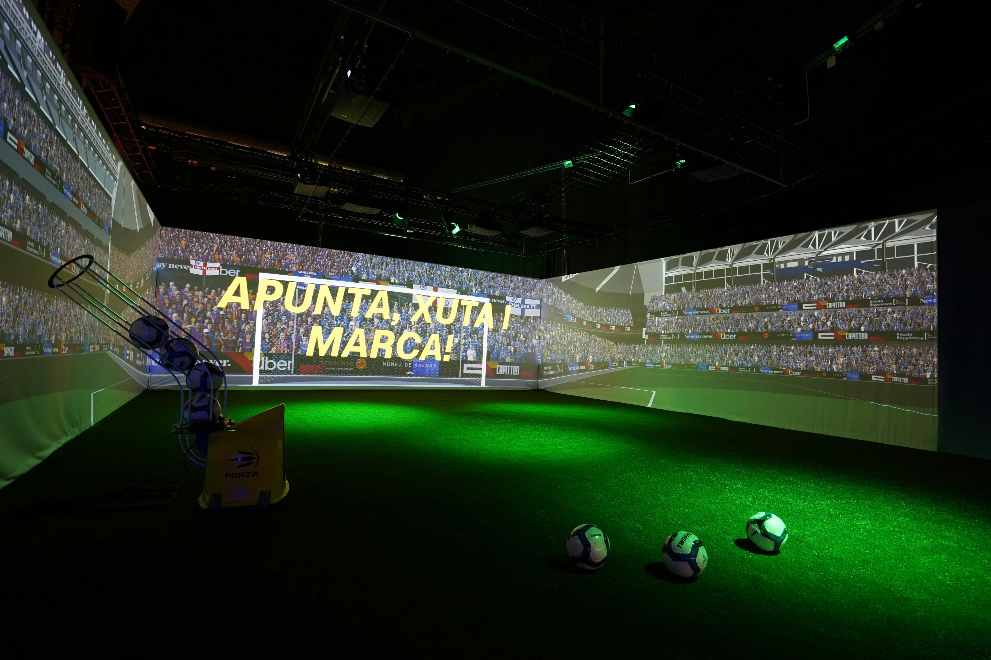A soccer-themed interactive display featuring a projection of a stadium, artificial turf, and soccer balls on the ground.