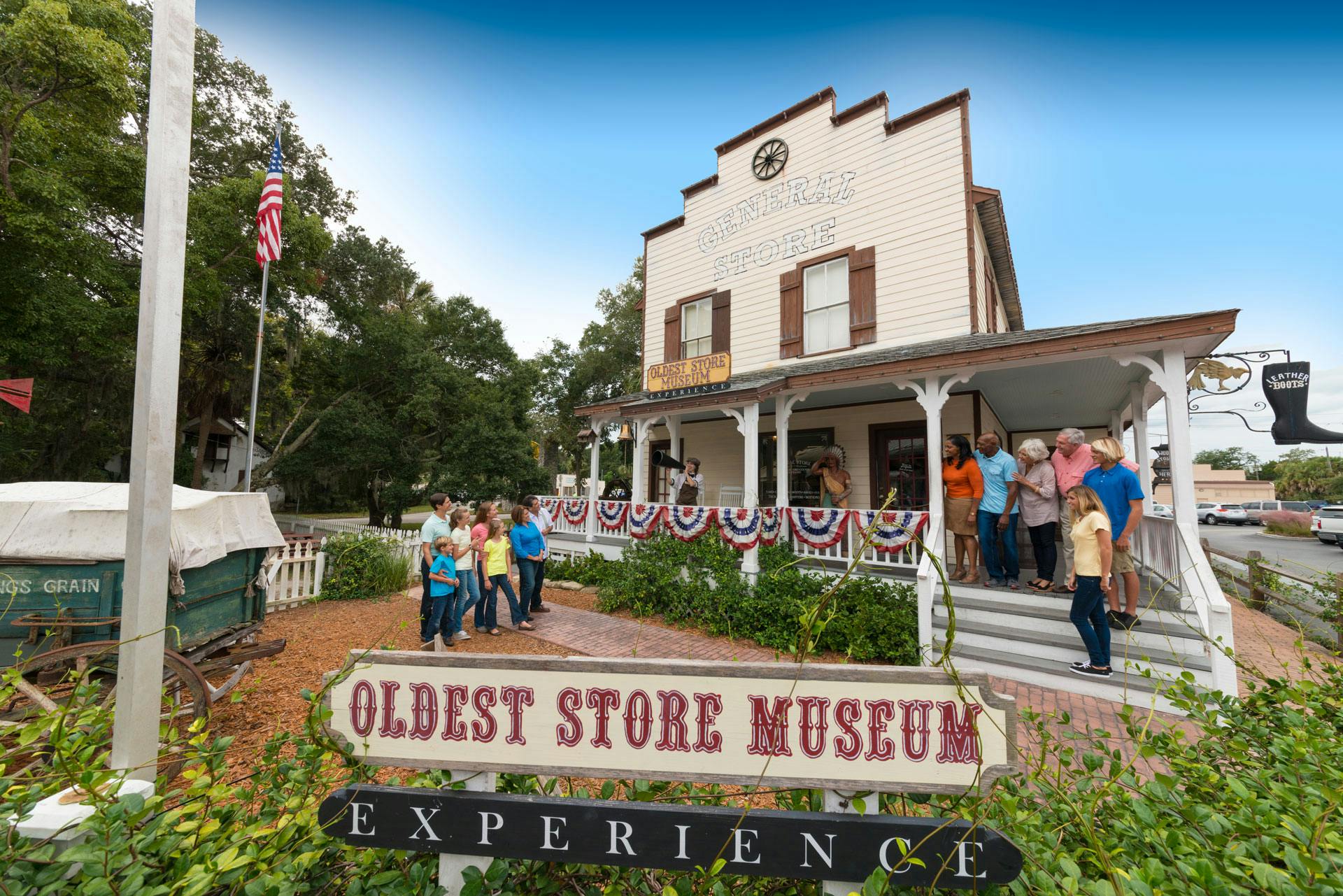 A group of people stands outside a historic building labeled "Oldest Store Museum Experience" with patriotic bunting on the porch.