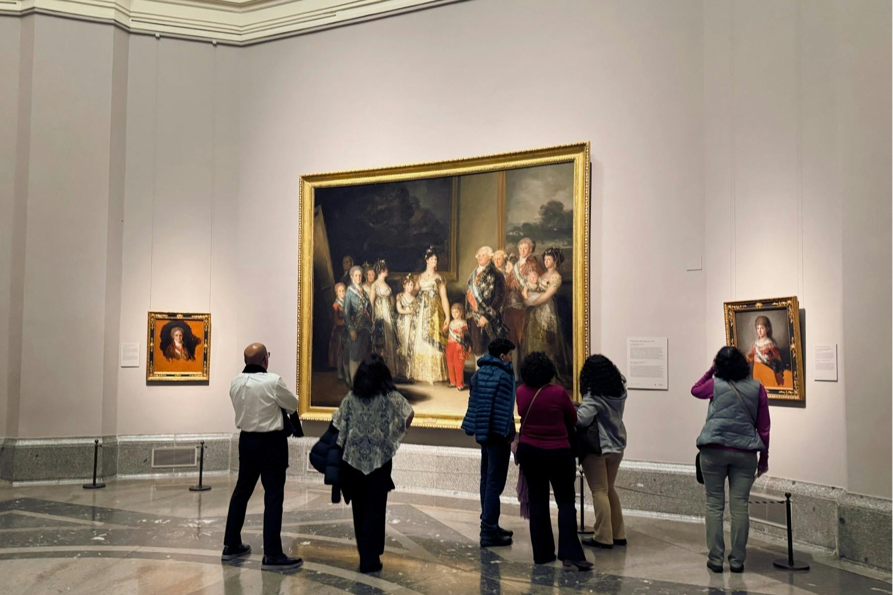 博物館を訪れる人々のグループが、ゴヤのチャールズ4世とその家族の王室の肖像画の前に立っています。