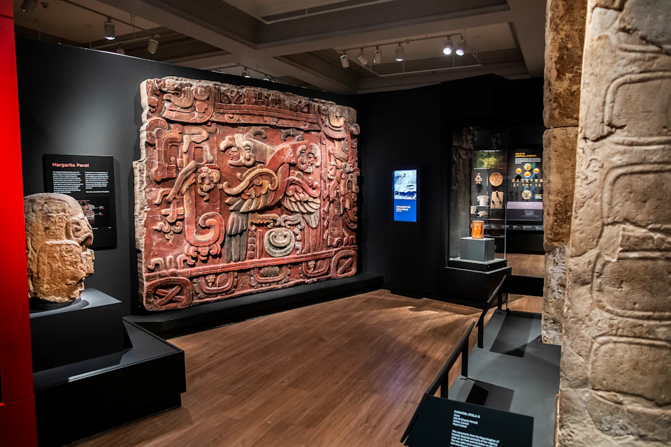 A museum exhibit showcasing a large, intricate, red and black ancient stone carving and informational displays under soft lighting.