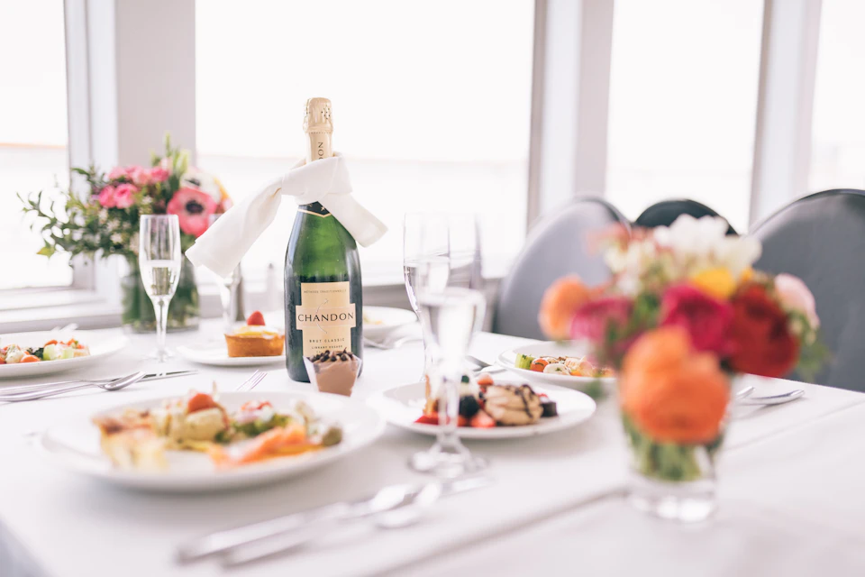 Elegant table setting with a Chandon champagne bottle, glasses, plates of gourmet food, and a colorful flower centerpiece.