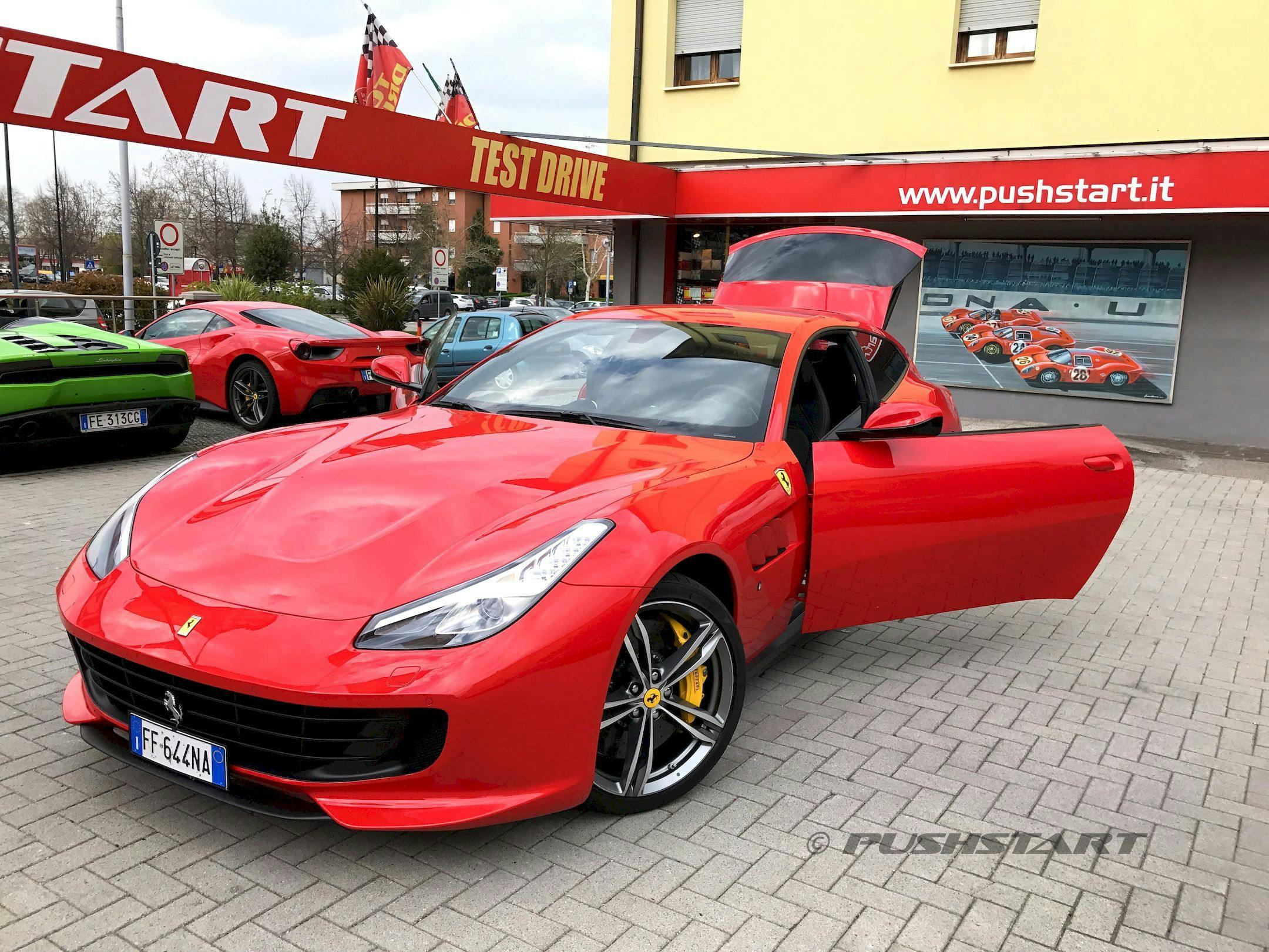 红色法拉利，车门敞开，后舱门凸起，停在试驾中心前。