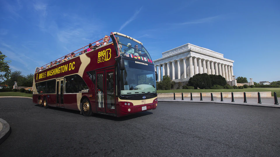 Double-decker sightseeing bus in front of the Lincoln Memorial in Washington, D.C., under a clear blue sky.