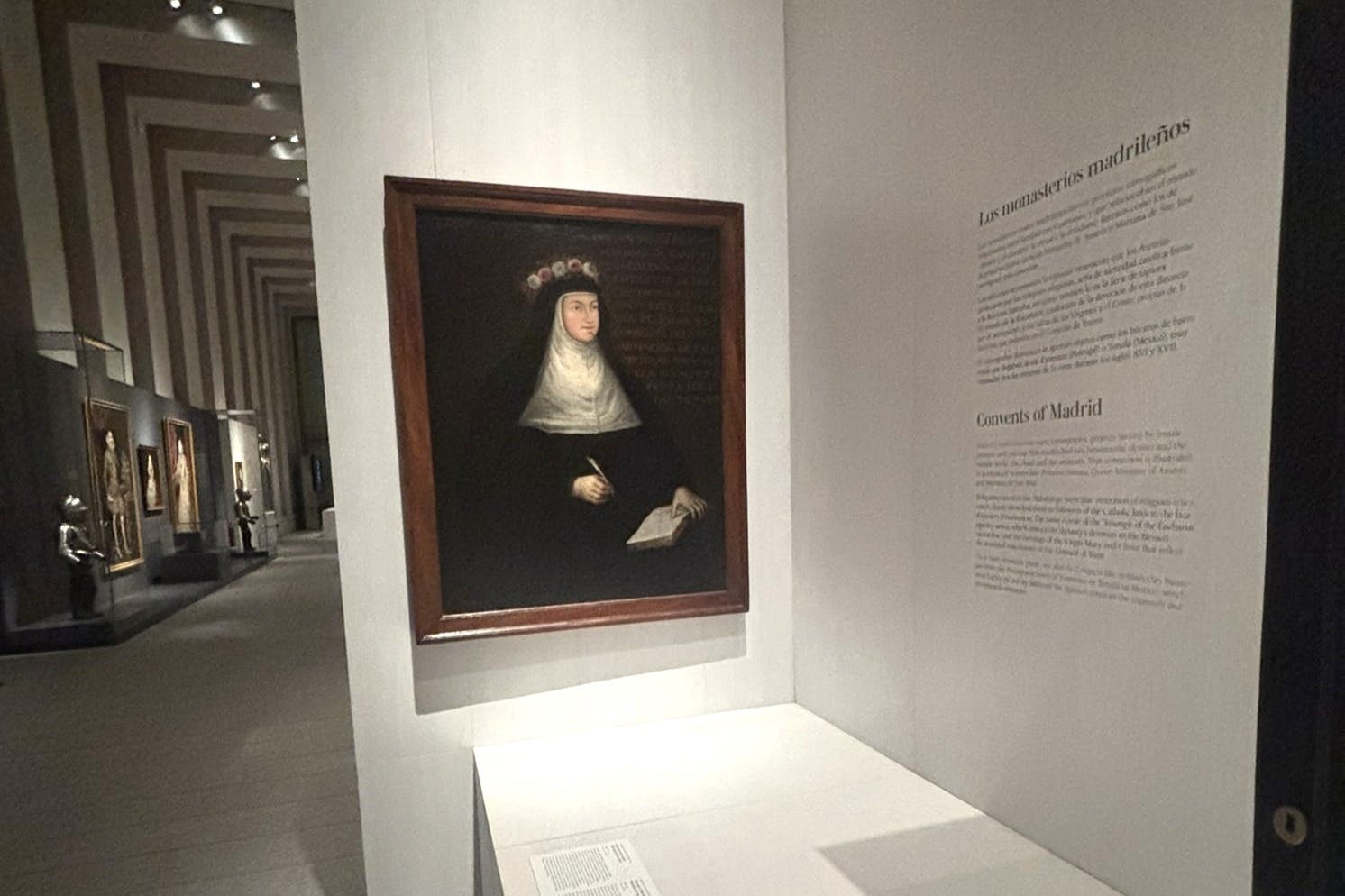 壁にテキストパネルがある美術館のギャラリーに展示されている、本を持った尼僧の額入りの肖像画。