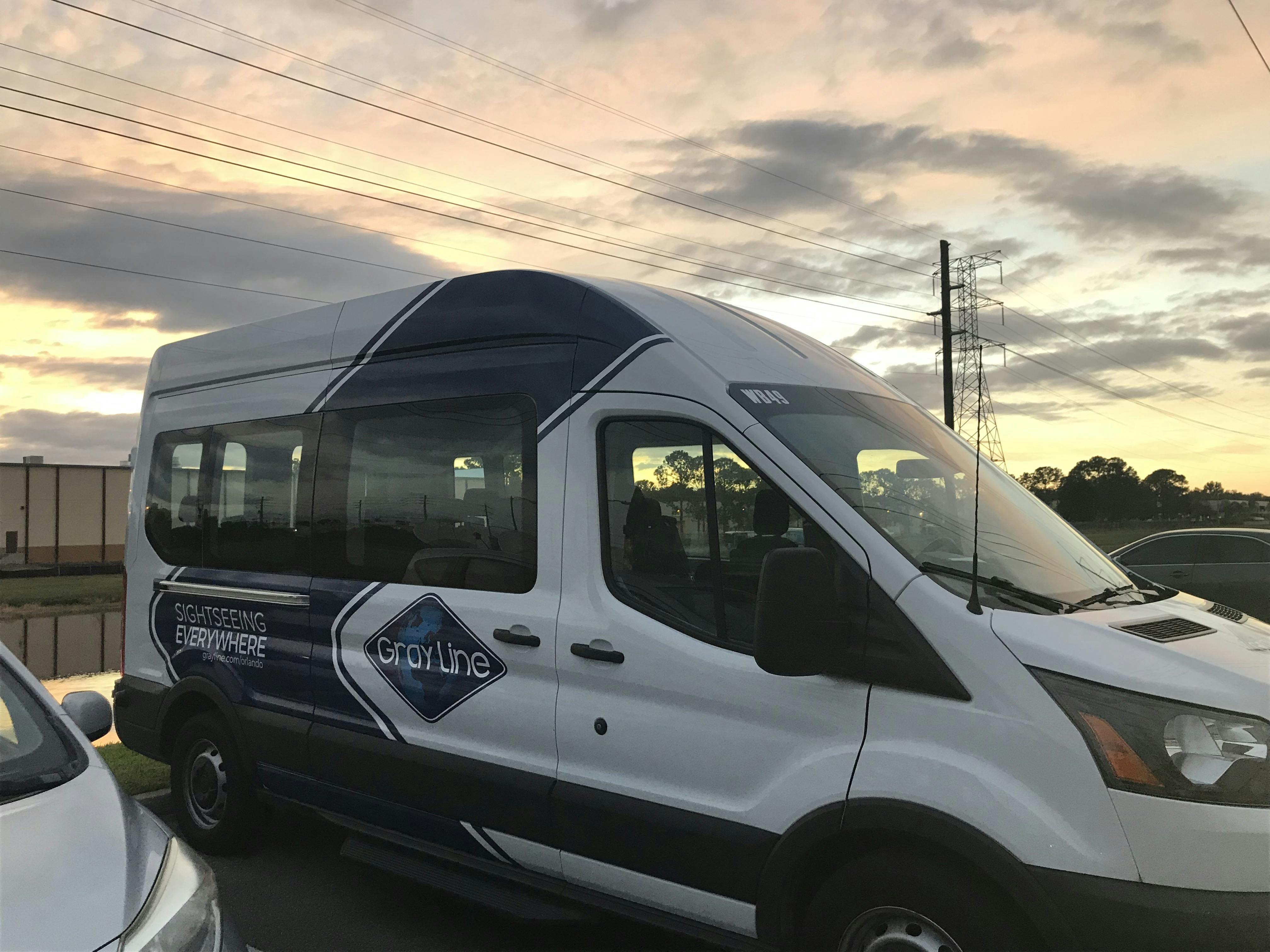 A white passenger van labeled "Gray Line" with "Sightseeing Everywhere" on its side, parked under a cloudy sunset sky.