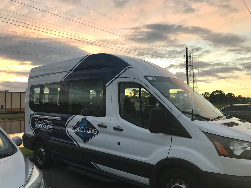 A white passenger van labeled "Gray Line" with "Sightseeing Everywhere" on its side, parked under a cloudy sunset sky.